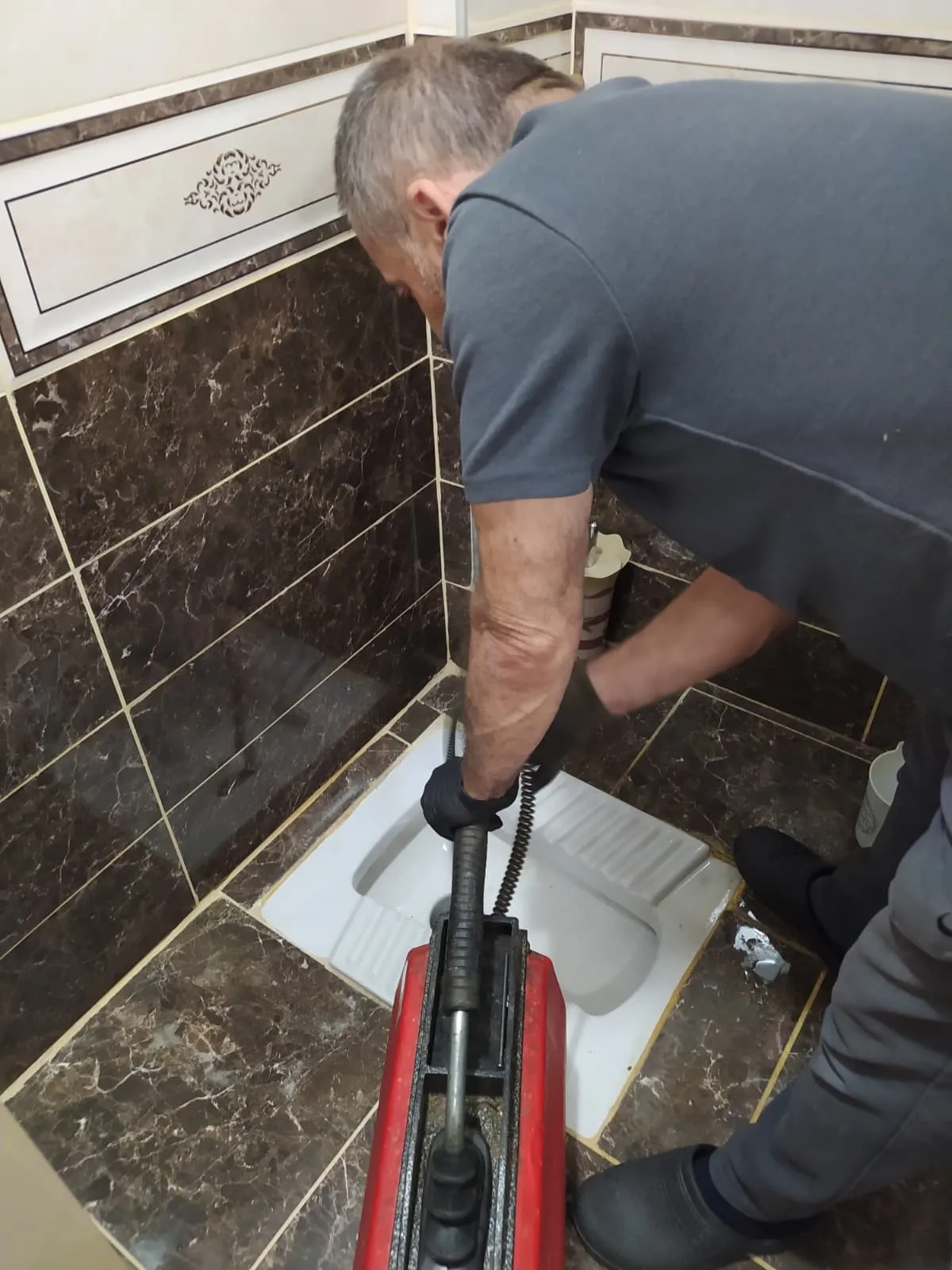Banyo giderinde tıkanıklık açma makinesi ile çalışan usta